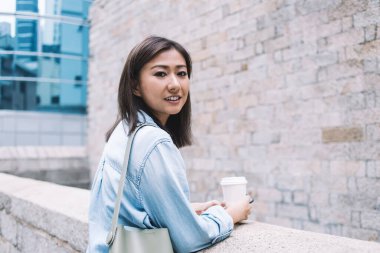 Gündüz vakti sokakta tuğla duvarın yanında dikilmiş gülümseyen ve yemek servisi yapan Asyalı genç bir kadının yan görünüşü.