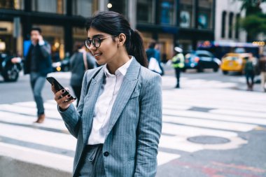 Optik göz giysisi içinde resmi giyinmiş işyeri sahibi, finansal raporla gelen e-postayı okuyor, akıllı telefon uygulaması üzerinden iletişim numarasını arayan klasik gözlüklü akıllı kadın tüccar.