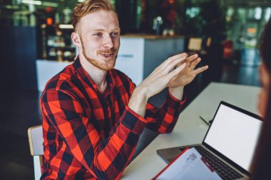 Yazılım geliştirme hakkında bilgi veren beyaz tenli olumlu bir adam yanında oturan başarılı meslektaşlarına dizüstü bilgisayarla bilgisayar başında sohbet ederken mutlu oluyor.