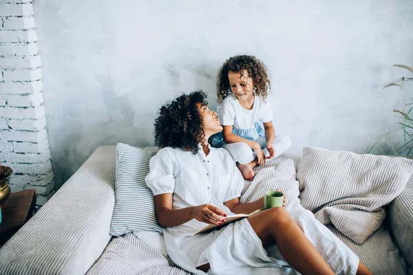 Kitap ve çayla kıvırcık bir kadın kanepede oturup tatlı bir kızın evde birlikte vakit geçirmesini izliyor.