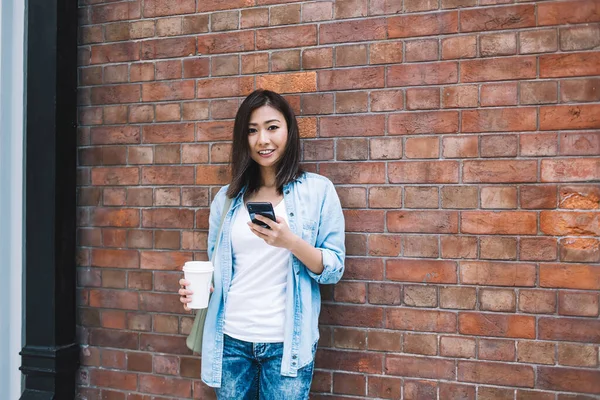 Wesoła Azjatka Dżinsach Odzież Stojąca Obok Ściany Filiżanką Kawy Smartfonem — Zdjęcie stockowe