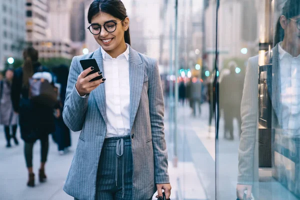 Finansal bölgede iş molası sırasında cep telefonuyla sanal iletişimden keyif alan pozitif kadın girişimci, klasik gözlüklü mutlu kadın paylaşımı için içerik metni yazıyor