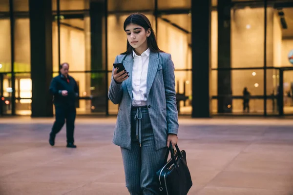 現代的なオフィスビルの前に立っている間 スマートフォン上の革のバッグメッセージングと正式な服の民族の美しい実業家 — ストック写真
