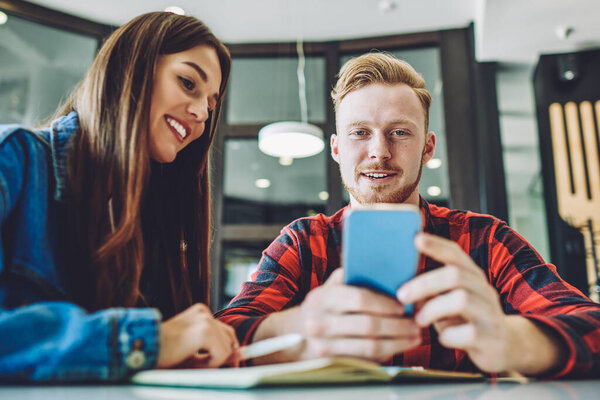 Улыбчивые студенты, отдыхающие от учебы на открытой площадке и общающиеся с друзьями через мобильное приложение для связи с помощью беспроводной связи 4g в помещении