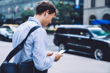 Klasik mavi tişörtlü ve kablosuz kulaklıklı erkek işçilerin arka planı sokakta telefonla mesajlaşmaları.