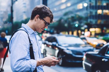 New York şehrinin arka planında duran yetişkin ve modern bir adamın cep telefonuyla sohbet edişinin yan görüntüsü 