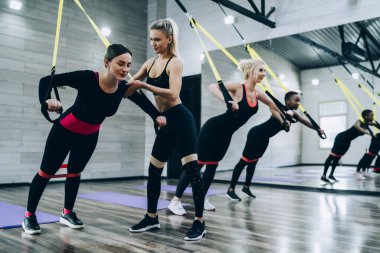 Kadın koçun dikilip, esmer esmerleri desteklerken, fitness kulübündeki çok ırklı kadınların yakınındaki genişletme ve direniş bandıyla aynaya doğru iterken yan görüntüsü.