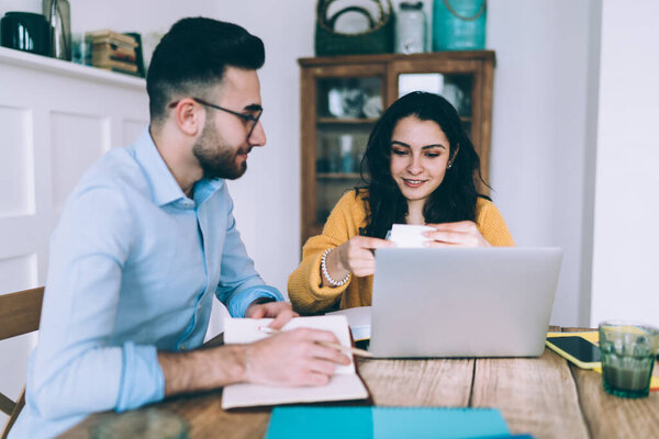 Молодые этнические мужчины и женщины в повседневной одежде фрилансеры, работающие вместе, подбирая материал для общей инициативы и улыбаясь дома