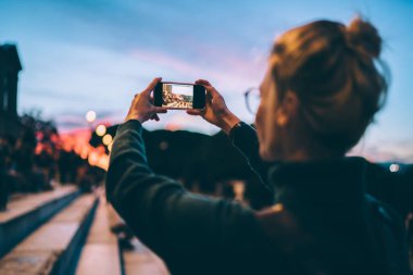 Hippi kızın akıllı telefon uygulaması ile şehrin fotoğraflarını çektiği arka plan görüntüsü 4G 'ye bağlı cep telefonu uygulaması, geziler sırasında kadın neslinin fotoğraflarını çektiği manzara.