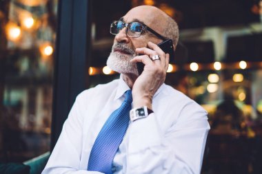 Gözlüklü, takım elbiseli, beyaz tişörtlü, camlara bakmadan telefonda konuşan kıdemli kısa saçlı adam.