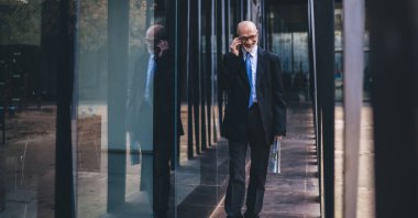 Resmi kıyafet ve gözlüklerle gülümseyen yaşlı bir işadamı ve elinde beyaz sakalla sokakta yürürken telefonla arayan bir gazete.