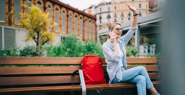 Delighted Student Trendy Clothes Eyeglasses Sitting Wooden Bench Waving Hand — Stock Photo, Image