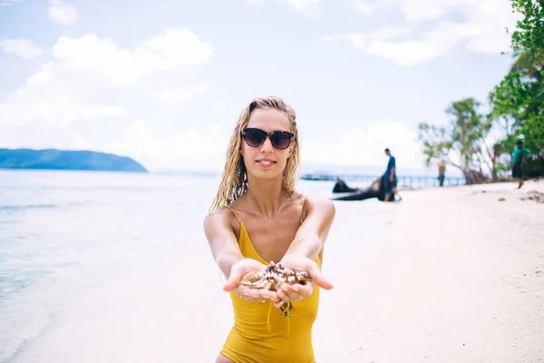 Junge Lächelnde Blondine Gelben Badeanzug Sitzt Und Zeigt Muschel Strand — Stockfoto