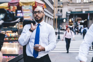 Kel sakallı, beyaz gömlekli, mavi kravatlı, omuzunda ceketi olan ve akıllı telefon kullanırken yüzünü çeviren Amerikalı patron.