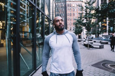 Spor kıyafetli, kel, Amerikalı bir erkek. Kulaklıkla müzik dinliyor. Modern ofis binasının yakınındaki sokakta antrenman yaparken gözlerini kaçırıyor.