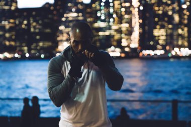 Eşofmanlı ve siyah eldivenli kaslı Afro-Amerikan bir adam arka planı yumrukluyor. 