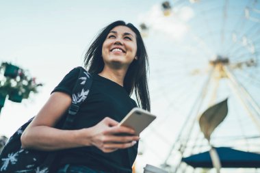 Elinde cep telefonu olan çekici, gülümseyen bir kadın elinde aletle dışarıda durup gülüyor ve eğlence parkında mutlu bir gün geçiriyor. Akıllı telefonlu mutlu bir hippi kız.
