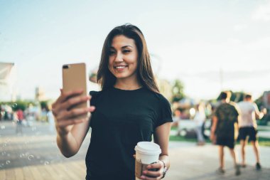 Gülümseyen hippi gezgin kahveyle cep telefonu kamerasıyla selfie çekerken havada kabarcıklar uçuşuyor, neşeli kadın etkili internete paylaşmak için komik videolar çekiyor.