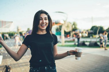 Boş tişörtlü mutlu bir kadın elinde yemek fincanı tutuyor ve lunaparkta eğleniyor, neşeli Asyalı hippi kız halka açık bir yerde eğlence gününde neşeli bir ruh hali içinde.