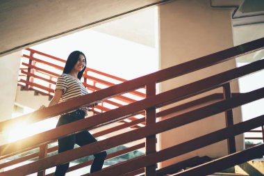 Moda giyinmiş hippi kız şehir binasının merdivenlerine tırmanıyor ve güneşli yaz gününde kendini iyi hissediyor. Zengin Asyalı kadın milenyumu şık giysiler içinde boş zamanların tadını çıkarıyor.