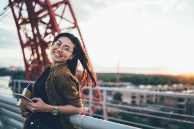 Şık gözlüklü komik Asyalı yeniyetme kızın yarım boy portresi şehir ortamından keyif alıyor, modern cep telefonu cihazlı kadın ağ kurmak ve web sitesini tarıyor.
