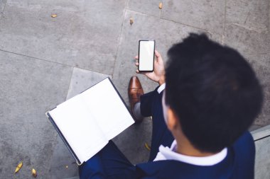Çağdaş, siyah saçlı, takım elbiseli, açık havada bankta oturan, telefonda günlük mesajı tutan etnik bir adamın en iyi görüntüsü.