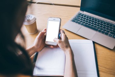 İnce kadın elleri Hong Kong 'da defter ve kahve fincanı ile ahşap masada modern akıllı telefona bakıyor.