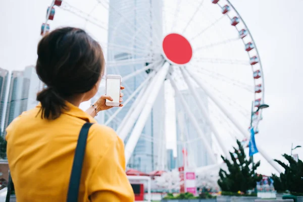 穿着休闲装 手持带有空白屏幕的智能手机 想象着香港街头公园的现代摩天轮的现代时尚女性的背景图 — 图库照片