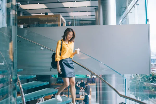若い笑顔明るいアジアの女性で黄色のシャツ黒革のスカートとバックパック移動階段で熱い飲み物と携帯電話で香港 — ストック写真