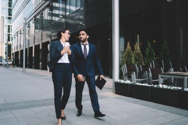Katı siyah takım elbiseli çok kültürlü iş arkadaşları yazın şehir merkezinde ellerinde cep telefonu klasörlü kahveyle yürüyorlar.