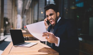 Saldırgan, ağlayan, siyah takım elbiseli, beyaz gömlekli, netbook 'ta sörf yapan iş adamı. Yaz kafeteryasında, ahşap masada oturan belgeleri kontrol ediyor.