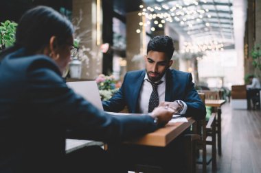 Resmi takım elbiseli düşünceli etnik erkek. Kravat inceleme raporu. Gözlüklü kadın kafede oturmuş projeyi tartışıyorlar.