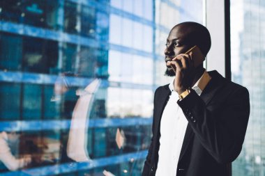 Kendinden emin, genç Afrikalı Amerikalı CEO telefonda konuşurken ve iş ortağıyla tartışırken çağdaş ofiste pencerede duruyordu.