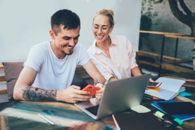 Gündüz vakti şık bir kafede ilham kaynağı bulmak için akıllı telefon ve defter kullanan gülümseyen genç iş arkadaşları.