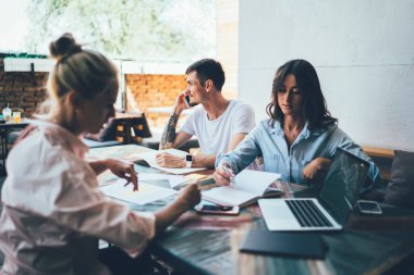 Arkadaşlar masada boş ekranlı dizüstü bilgisayarlarıyla otururken odaklanmış genç kadınlar yazılı planı ve akıllı telefondan konuşan adamı tartışıyor.
