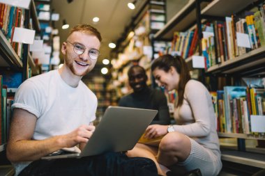 Kütüphane zemininde oturmuş, dizüstü bilgisayarı olan bir adam kameraya bakarken aynı anda hometask üzerinde çalışan çok ırklı, zeki öğrencilerden oluşan bir grup.