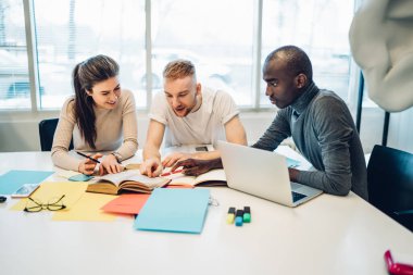 Bir grup çok ırklı iş arkadaşı ofis binasında Joy 'la çalışırken notlar yazıp dizüstü bilgisayar kullanıyorlar.