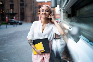 Sokakta cep telefonuyla konuşurken elinde not defterleri olan ve kameraya bakan aktif ve modaya uygun genç bir bayan.