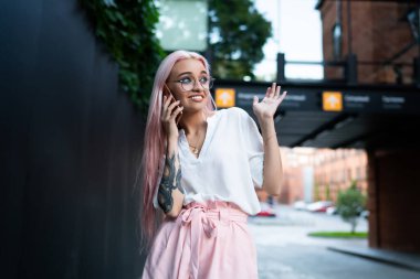 Uzun gül saçlı, şık yaz kıyafetleri giyen, moda gözlüklü, cep telefonu konuşmalarında şaşırmış, sokakta yürürken yüzünü çeviren genç ve çekici bir kadın.