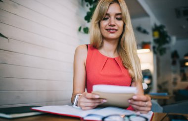 Alttan, sarı saçlı, konsantre genç ve çekici bir kadın. Kafede oturup çalışırken iş bilgisi alıyor ve okuyor.