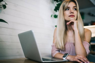 Genç, düşünceli, sarışın bir kadın. Çenesine eğilip, kafeteryada oturmuş dizüstü bilgisayarla çalışırken gözlerini kaçırıyor.