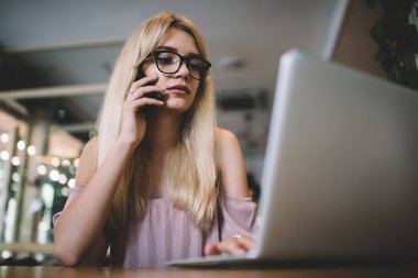 Genç sarışının gözlüklü, açık pembe elbiseli, telefonda konuşan ve internet kafede dizüstü bilgisayarda yazan düşük açılı görüntüleri.