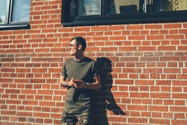 Elinde cep telefonu olan modaya uygun giyinmiş, elinde cep telefonu olan, şehrin duvarına bakarken gülümseyen, dijital aletli bin yıllık bir adam boş zamanlarında eğleniyor.