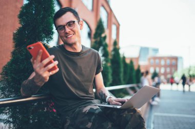 Cep telefonuyla 4G kablosuz internete bağlanan oyuncular için web sitesinde göz giysisi okuyan mutlu hippi adam cep telefonuyla web sayfalarını tarayan yetenekli, neşeli adam.