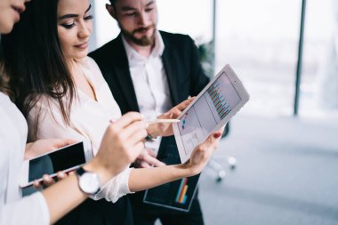 Resmi kıyafet giymiş bir grup ofis çalışanı, bulanık arka plandaki modern ofis binasındaki beyaz tablet üzerindeki finansal tabletleri analiz ediyor ve tartışıyorlar.