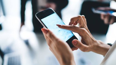Tanımlanamayan bir kadın ofis çalışanının elleri resmi giyinmiş meslektaşlarıyla gizli arka plandaki akıllı telefon uygulaması ile şifreli kişisel bilgilerini giriyor.