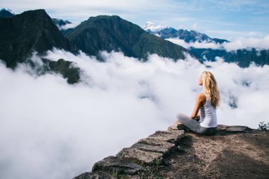 Sarı saçlı kadın nilüfer çiçeğinin kenarında oturuyor ve huzur ve huzur dolu bir ruh uyumu için ilham veriyor dağlara seyahat turunda ve Peru 'daki Machu Picchu bulutlarla kaplı