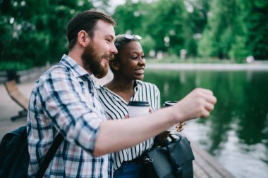 Genç, çoklu etnik çeşitliliğe sahip kadın ve erkek kahve içerek ve gün ortasında gölün kenarında komik sohbetler yaparak eğleniyorlar.