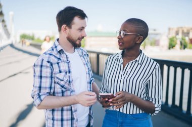 Kısa saçlı, gözlüklü, köprüde sakallı genç bir arkadaşla gezen Afrikalı Amerikalı bir kadın.