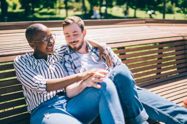Neşeli, şefkatli, çok ırklı bir çift. Geniş ahşap bankta oturup sarılıyorlar. Güneşin tadını çıkarıyorlar.